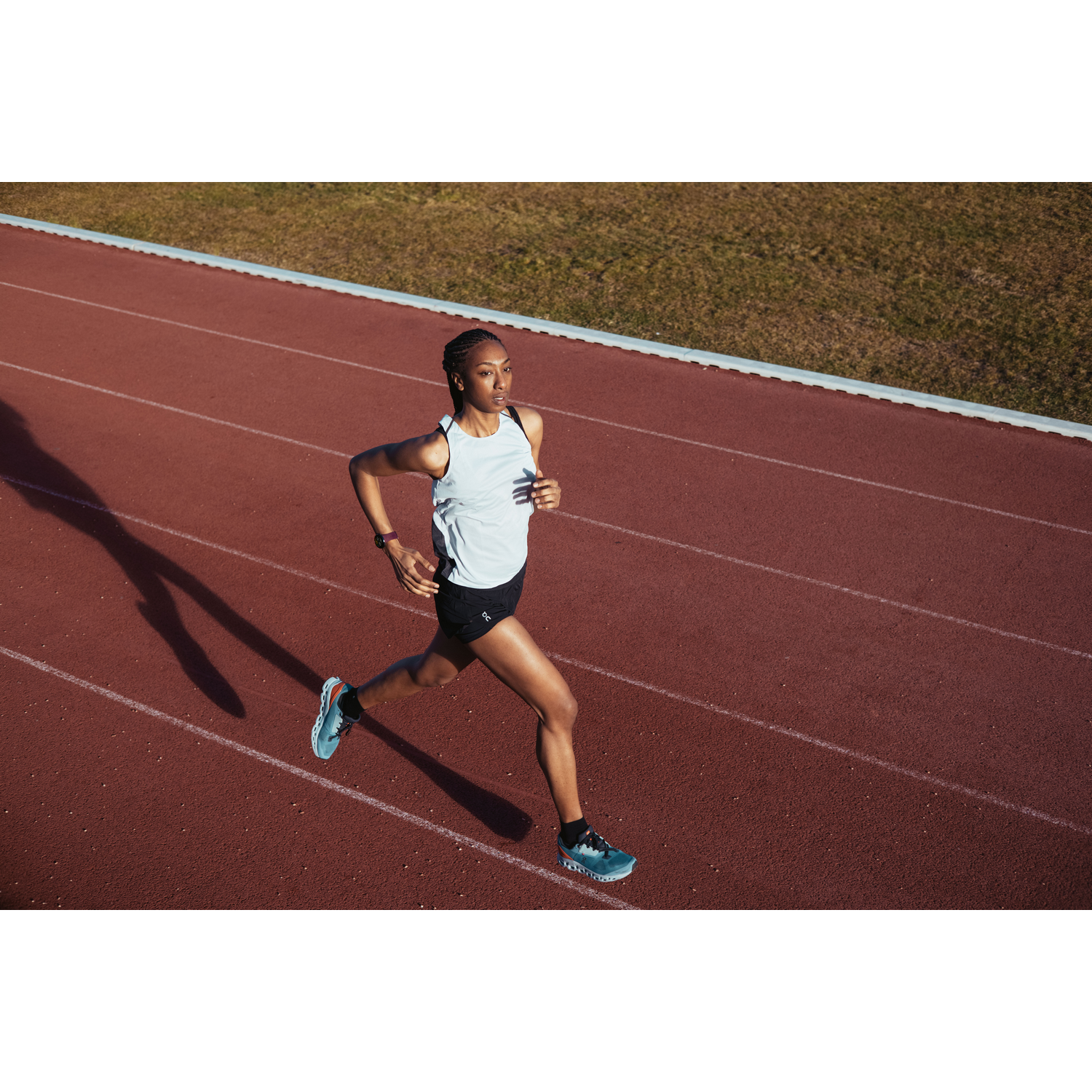 Atleta corriendo en una pista, con top blanco, shorts negros y zapatillas.