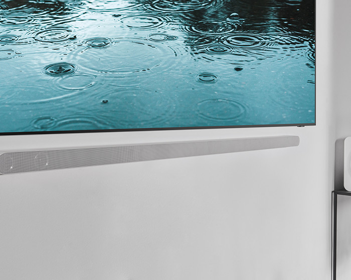 Een soundbar gemonteerd op een witte muur onder een tv.