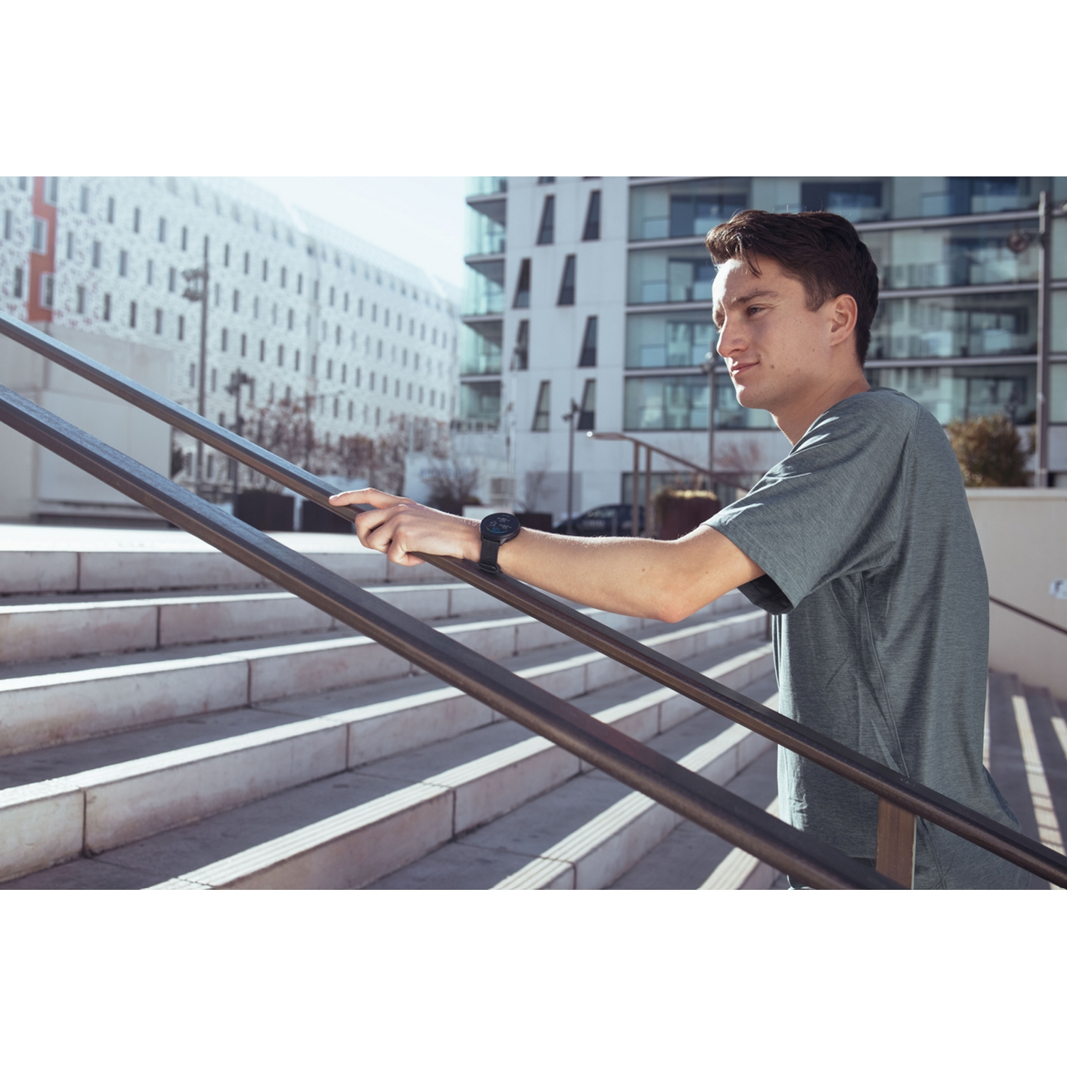 Un hombre subiendo escaleras, usando un reloj inteligente, en un entorno urbano con edificios modernos.