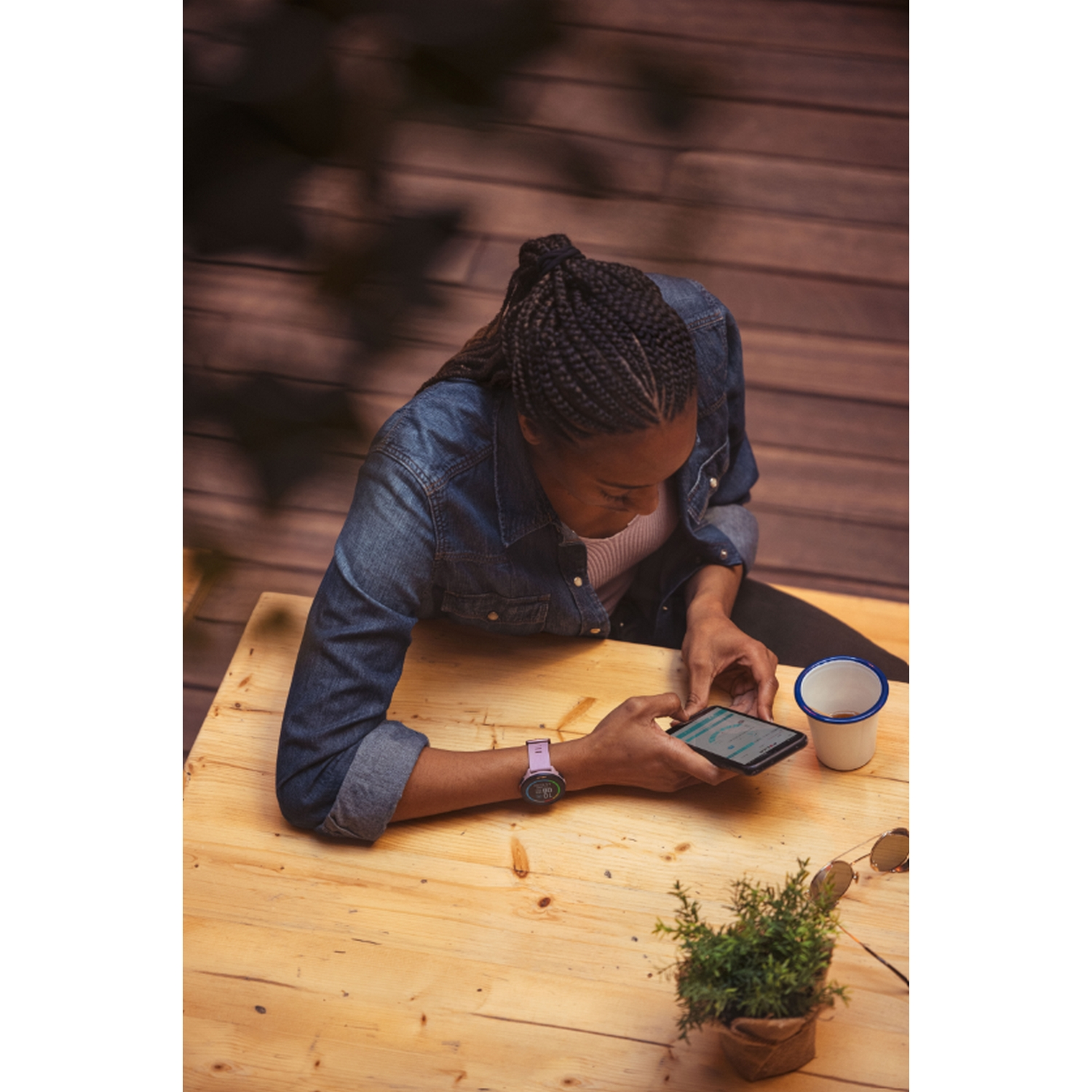 Persona con reloj inteligente y teléfono en una mesa de madera con una pequeña planta.