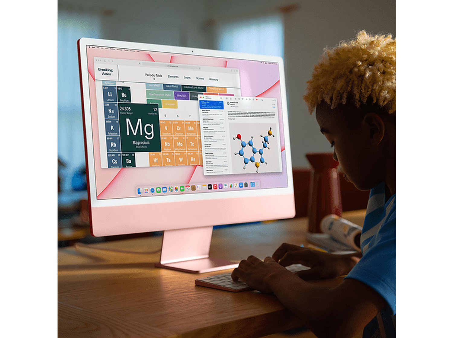 Un niño usa una computadora iMac rosa con un teclado rosa sobre una mesa de madera.