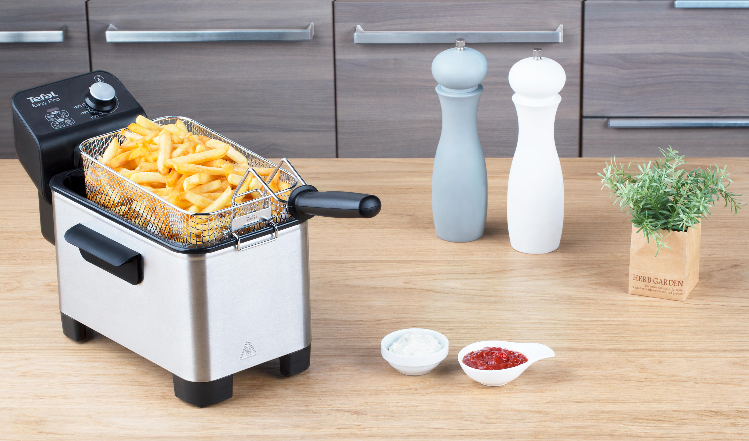 A silver deep fryer with a black basket full of fries, and condiments.