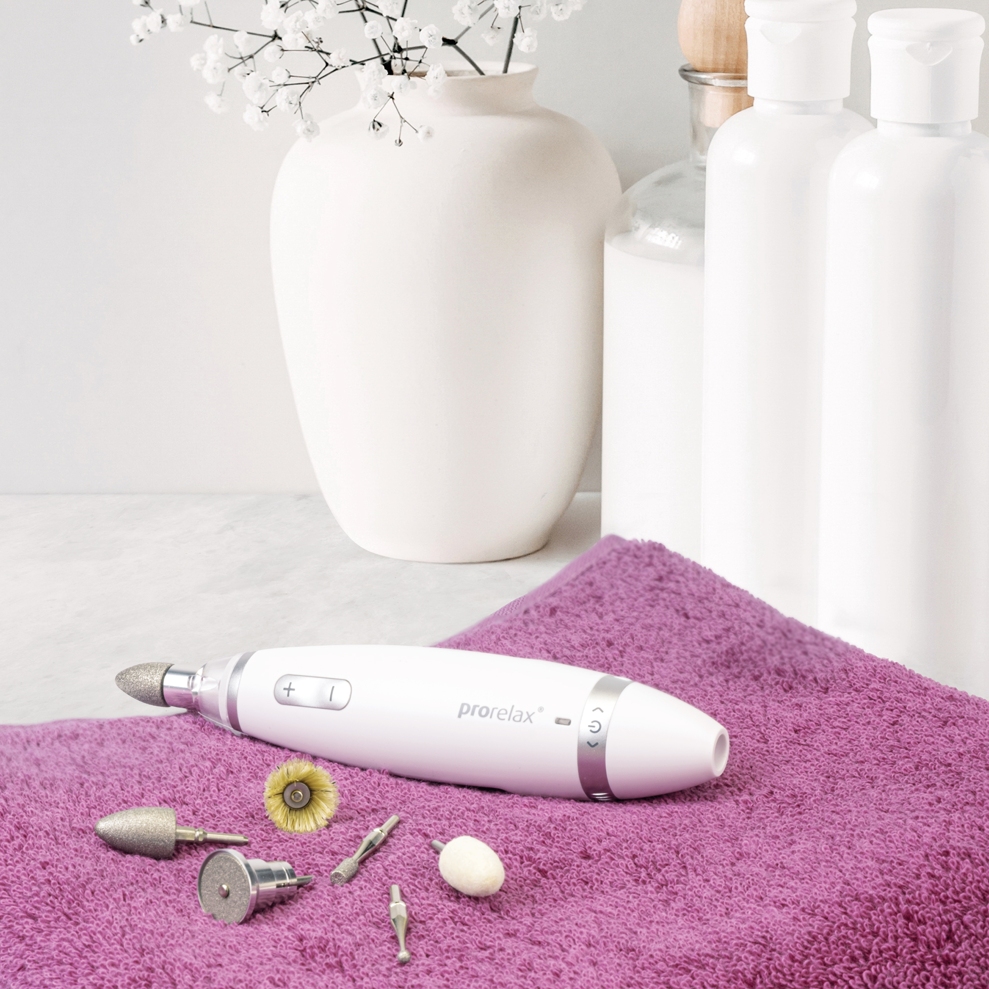 Ein weißes Maniküre-Werkzeug liegt auf einem lila Handtuch neben Werkzeugen und einer Vase mit Blumen.