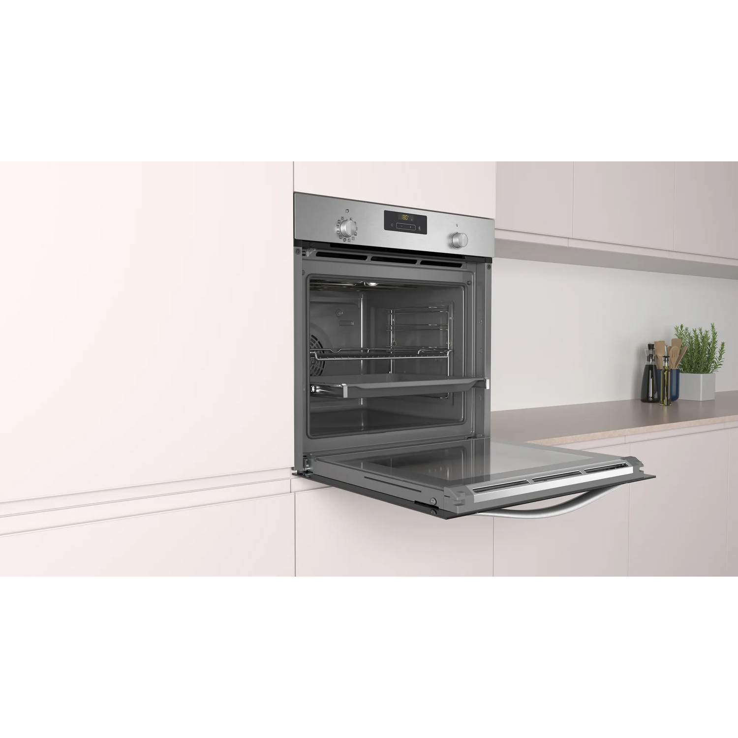 Un horno con la puerta abierta, acero inoxidable, en una cocina blanca con planta.