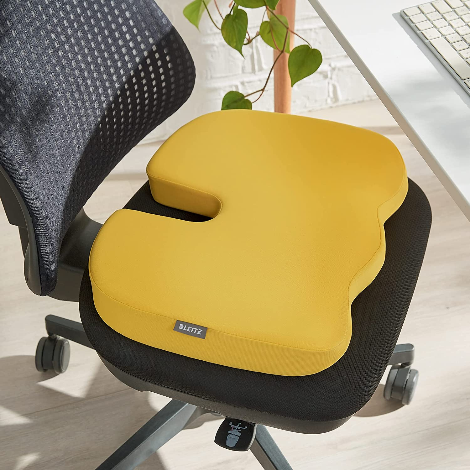Sárga ergonómikus párna egy fekete irodai széken. Egy növény a háttérben.
