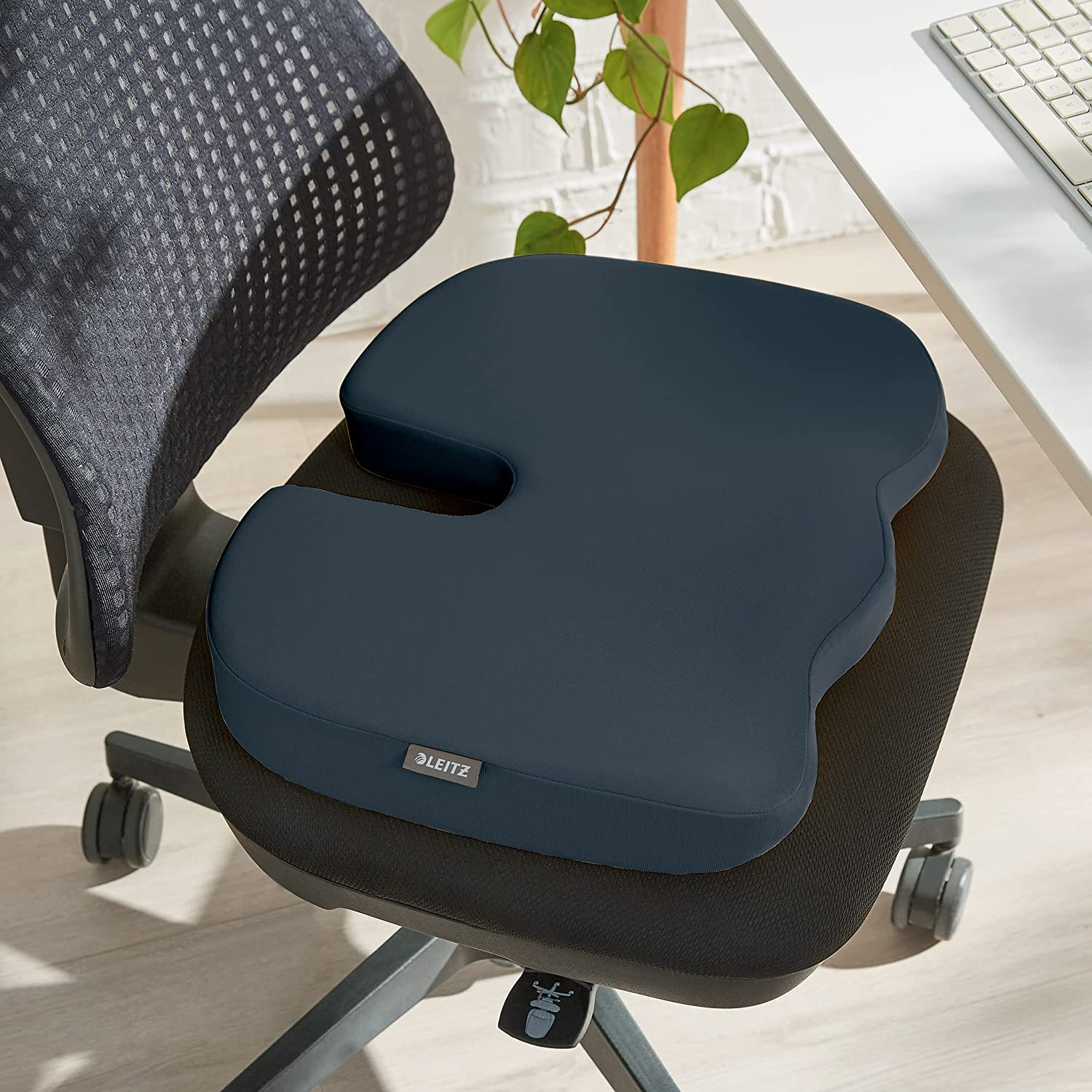 Egy kék ergonomikus párna egy fekete irodai széken. A széknek kerekei vannak.