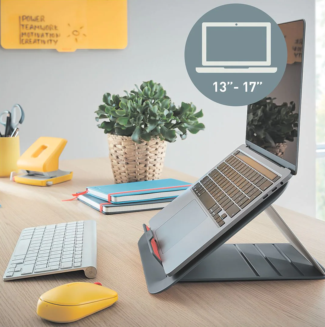 Laptop állványon sárga egérrel, billentyűzettel és más tárgyakkal egy fa asztalon.