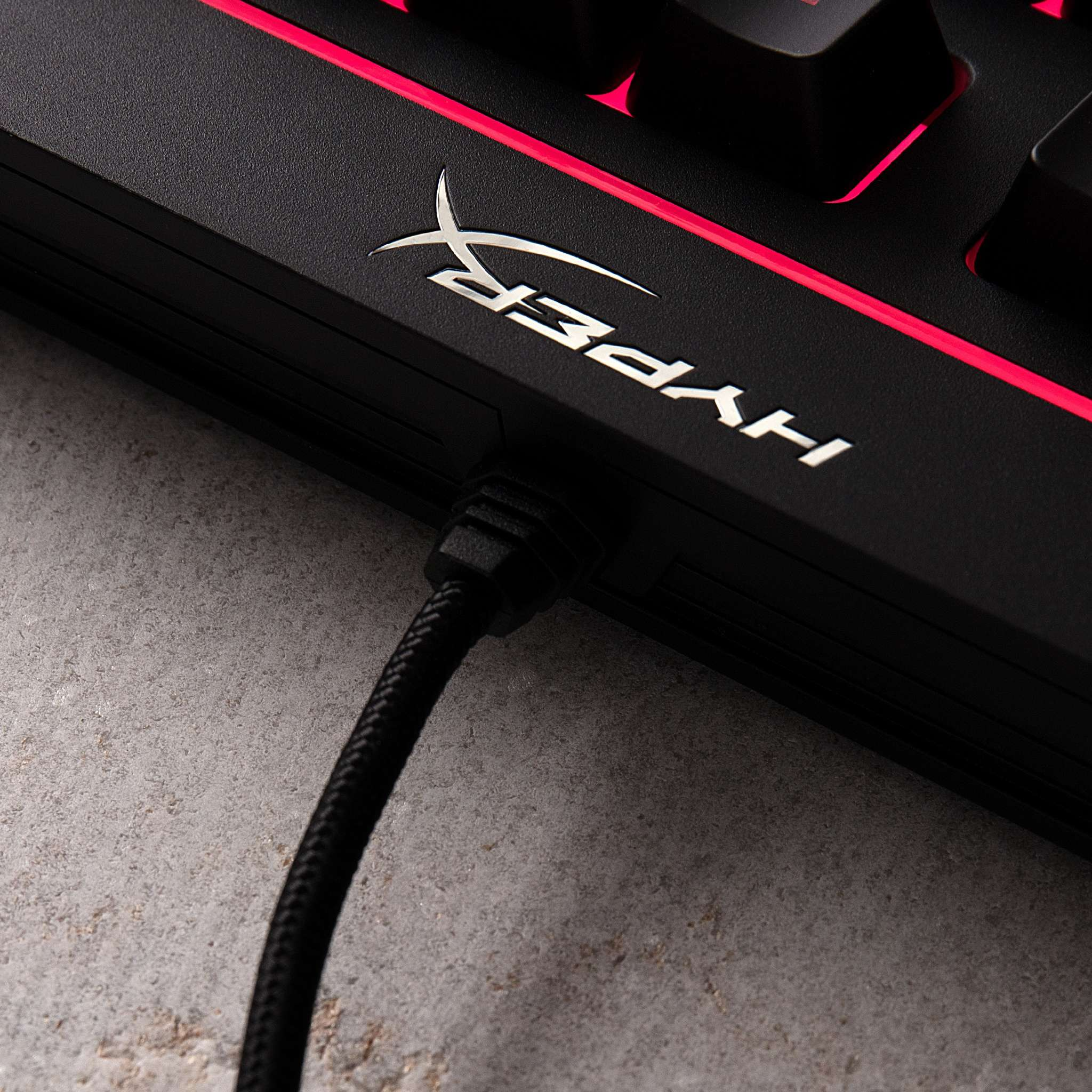 Close-up van een zwart toetsenbord met een USB-kabel aangesloten. De merknaam HYPERX is zichtbaar.