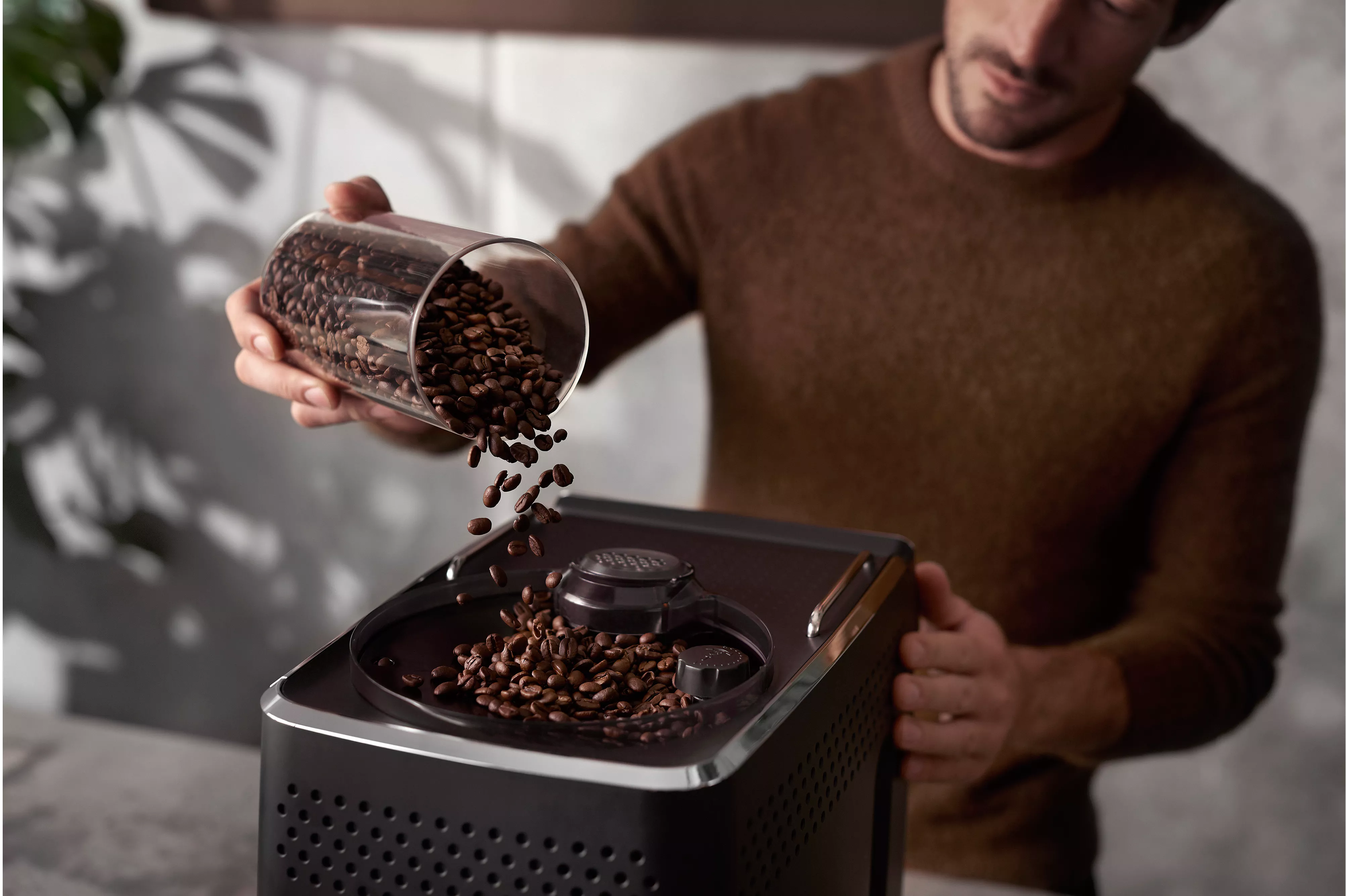 Uomo che versa chicchi di caffè in un macinacaffè, ripresa ravvicinata.