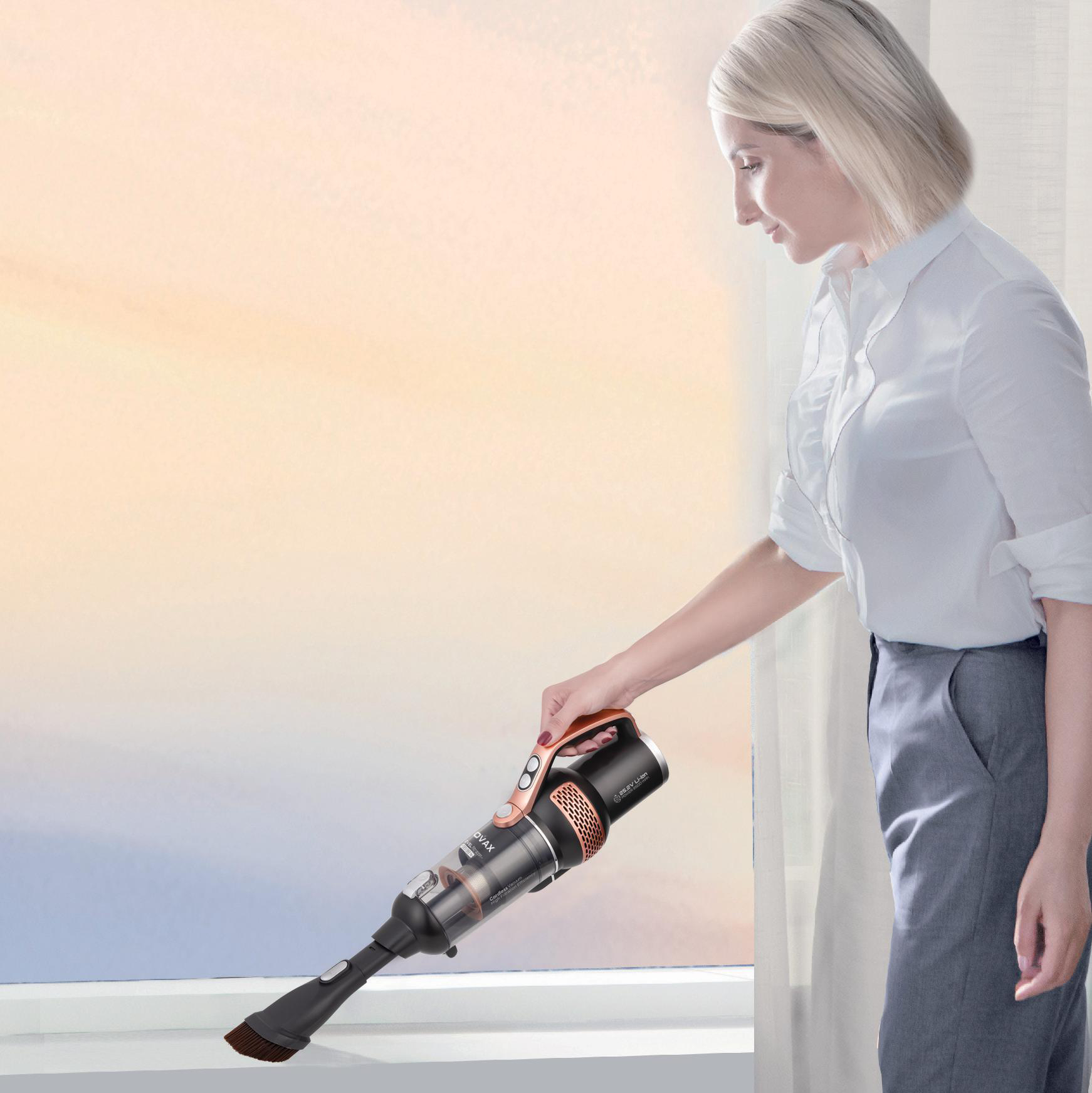 Eine Frau benutzt einen Handstaubsauger in der Nähe eines Fensters. Der Hintergrund ist eine Sonnenuntergangsszene.