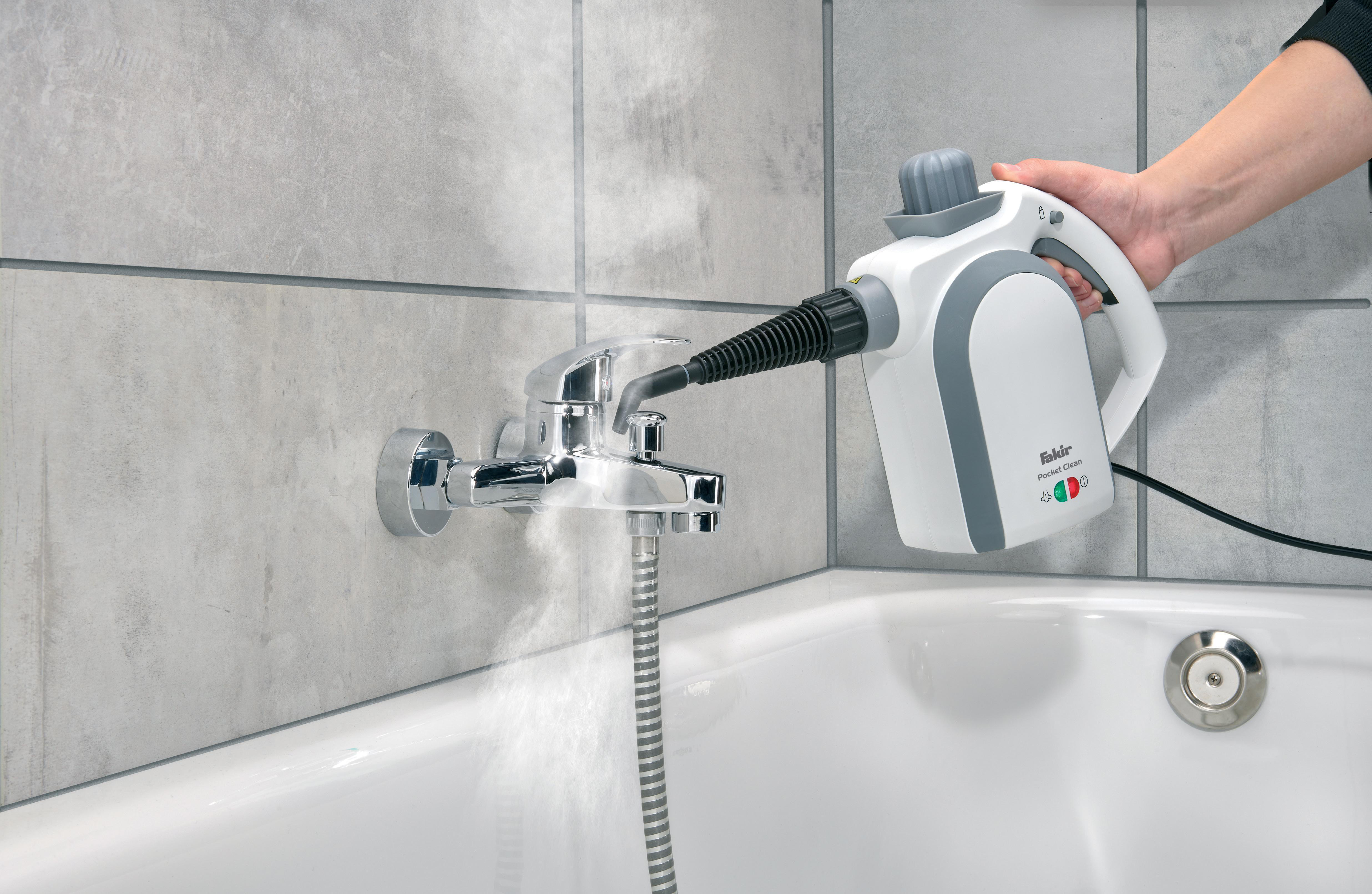 Eine Hand hält einen Dampfreiniger über einem Badewannen-Wasserhahn, Dampf ist sichtbar.