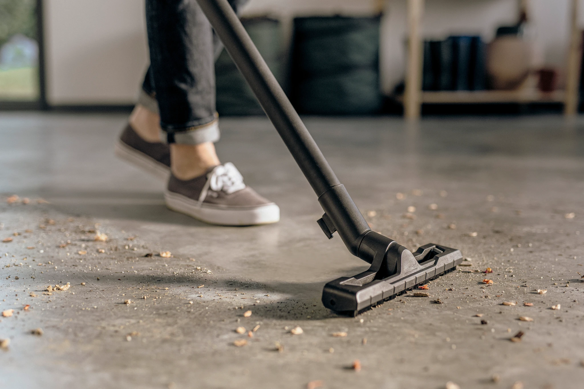 A person vacuums a floor with dirt and debris on it.