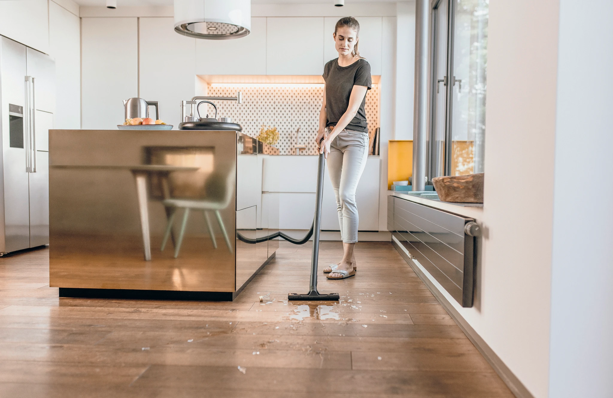 Woman vacuuming a wet floor in a kitchen with a stainless steel island.