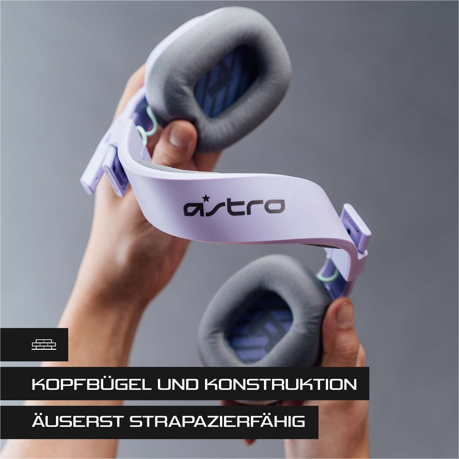 Eine Person hält ein helllila Astro-Gaming-Headset mit grauen Ohrmuscheln vor grauem Hintergrund. Text unten.