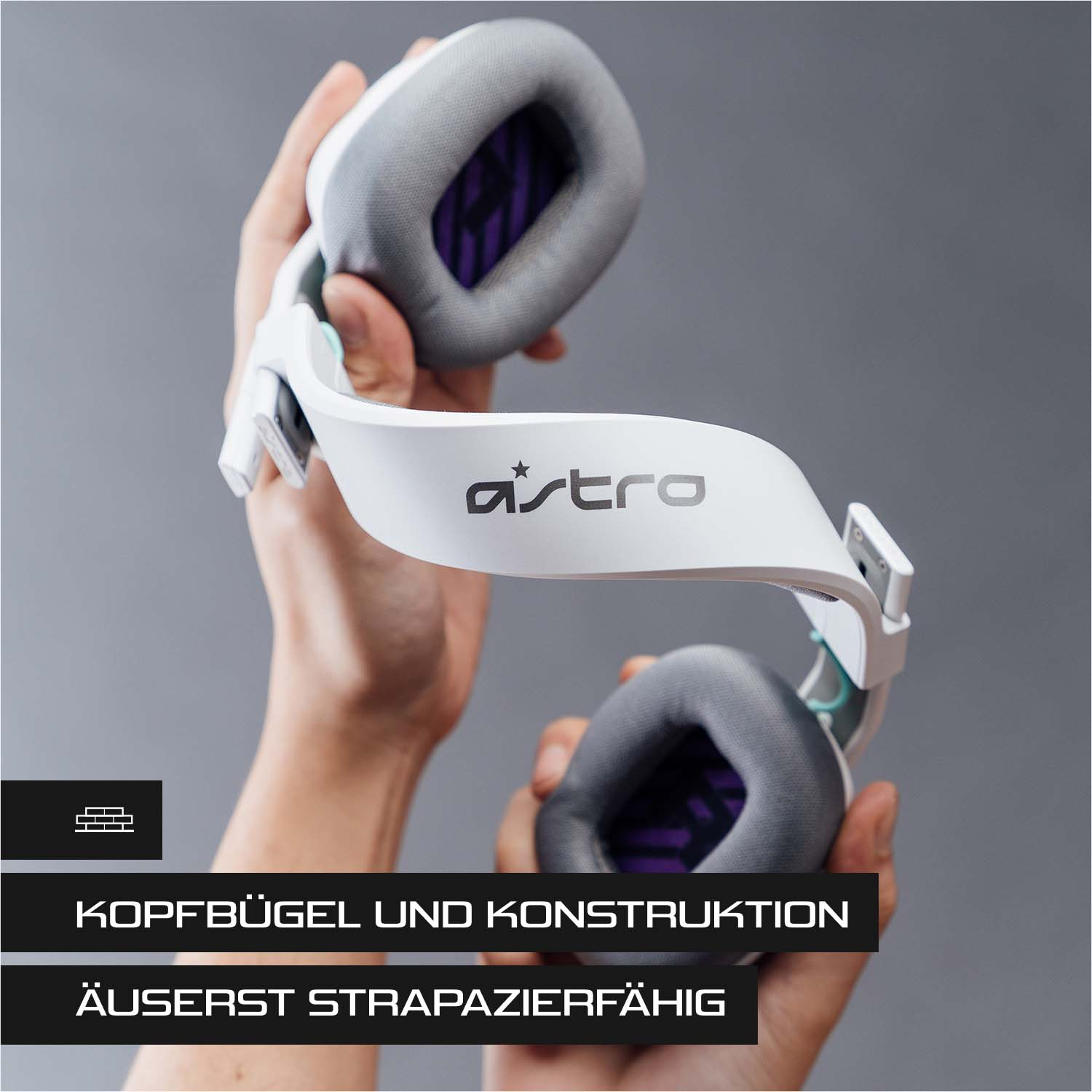 Ein weißes und graues Astro-Headset, das von Händen gehalten wird. Der Text lautet Kopfbugel.