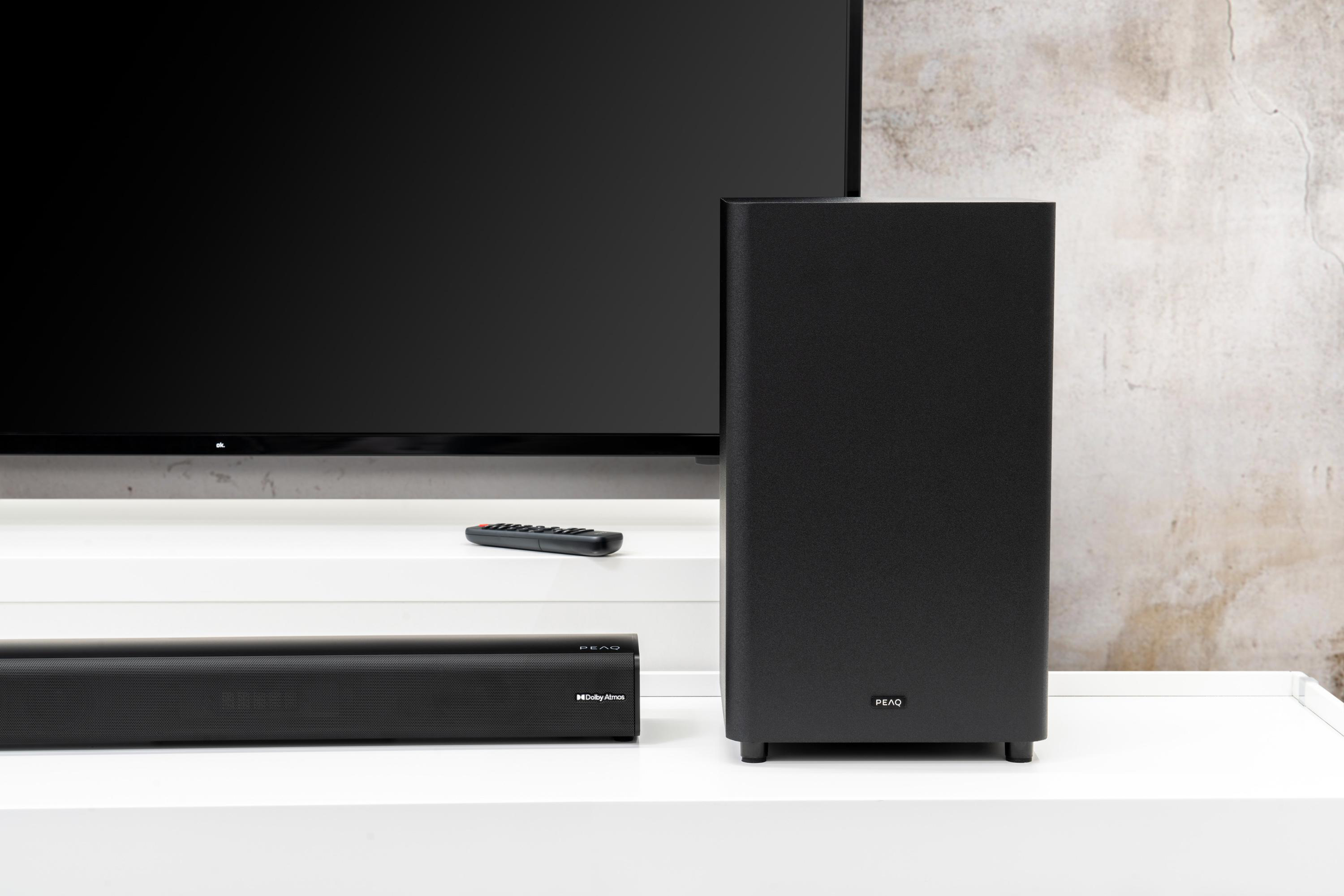 Schwarzer Fernseher, Soundbar und Subwoofer auf weißer Oberfläche, grauer Hintergrund.