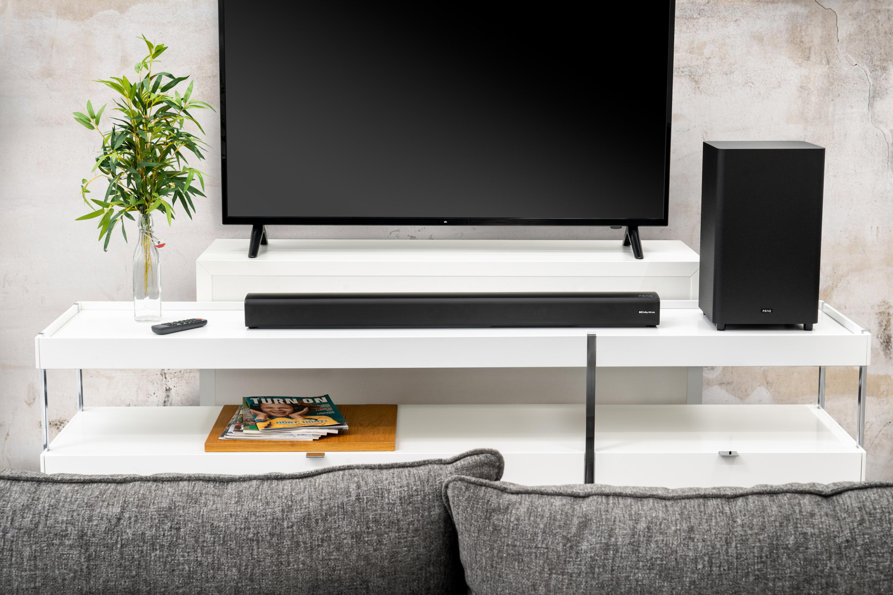 Fernseher, Soundbar und Subwoofer auf einem weißen Schrank. Ein Magazin und Pflanze.