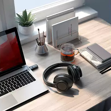 Un bureau avec un ordinateur portable, un casque, une tasse de thé, des livres, des crayons et une petite plante. La scène est bien éclairée.