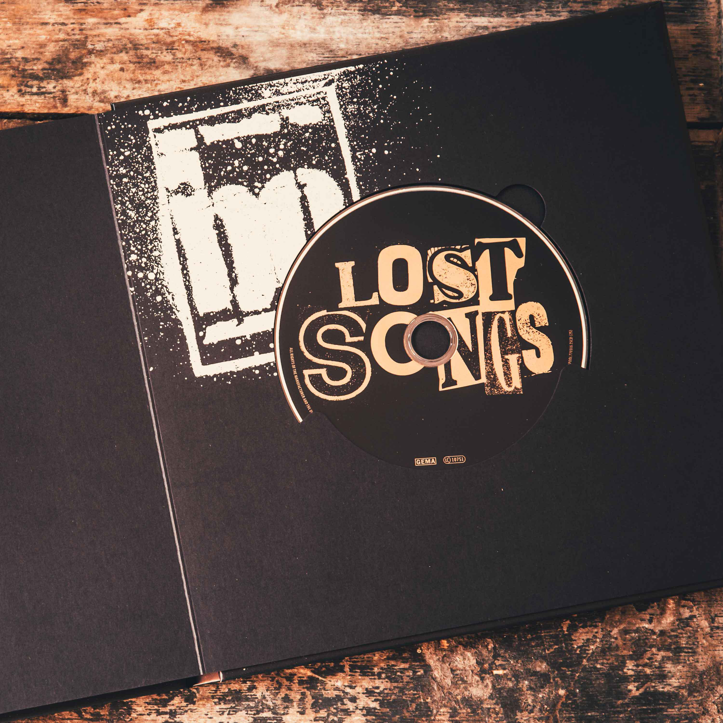 Geöffnete schwarze CD-Hülle, eine CD mit 'LOST SONGS' darauf, auf Holz.