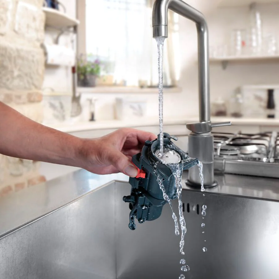 Eine Hand hält eine schwarze Maschine unter einem Wasserhahn mit fließendem Wasser über einem Waschbecken.