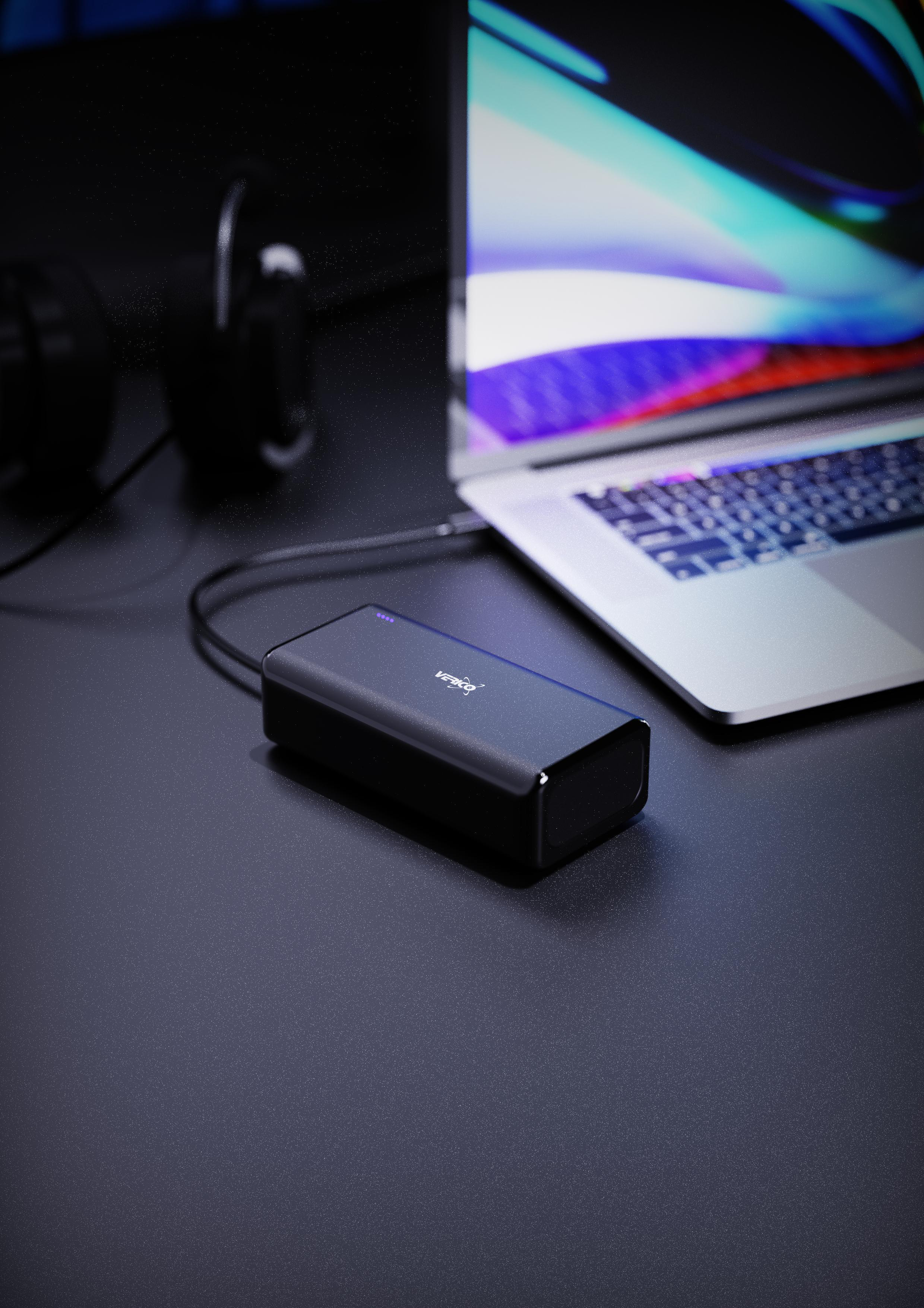 Laptop, Powerbank und Kopfhörer auf dunkler Oberfläche. Fokus liegt auf der Powerbank.