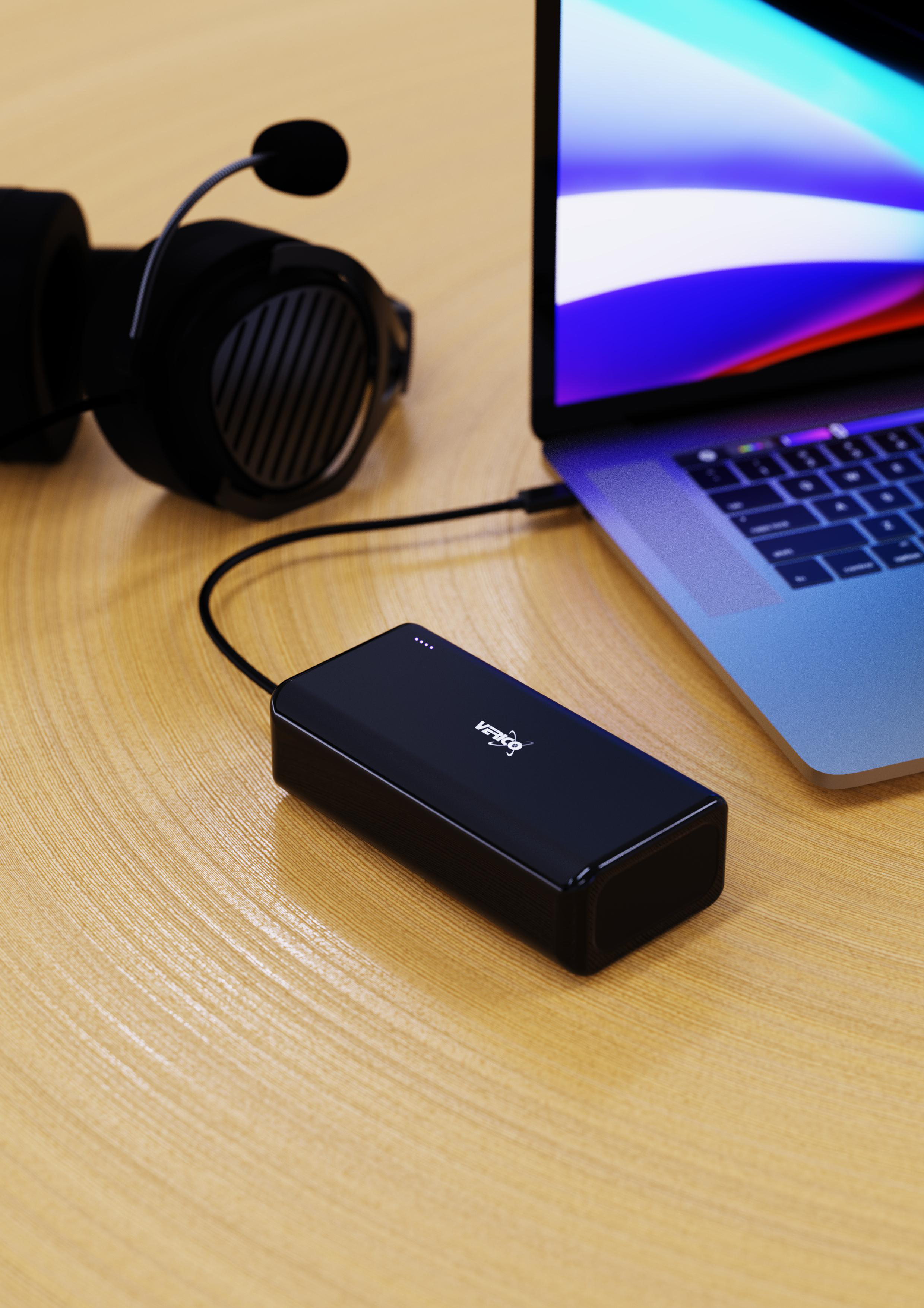 Eine schwarze Powerbank lädt einen Laptop, Kopfhörer auf einem Holztisch.