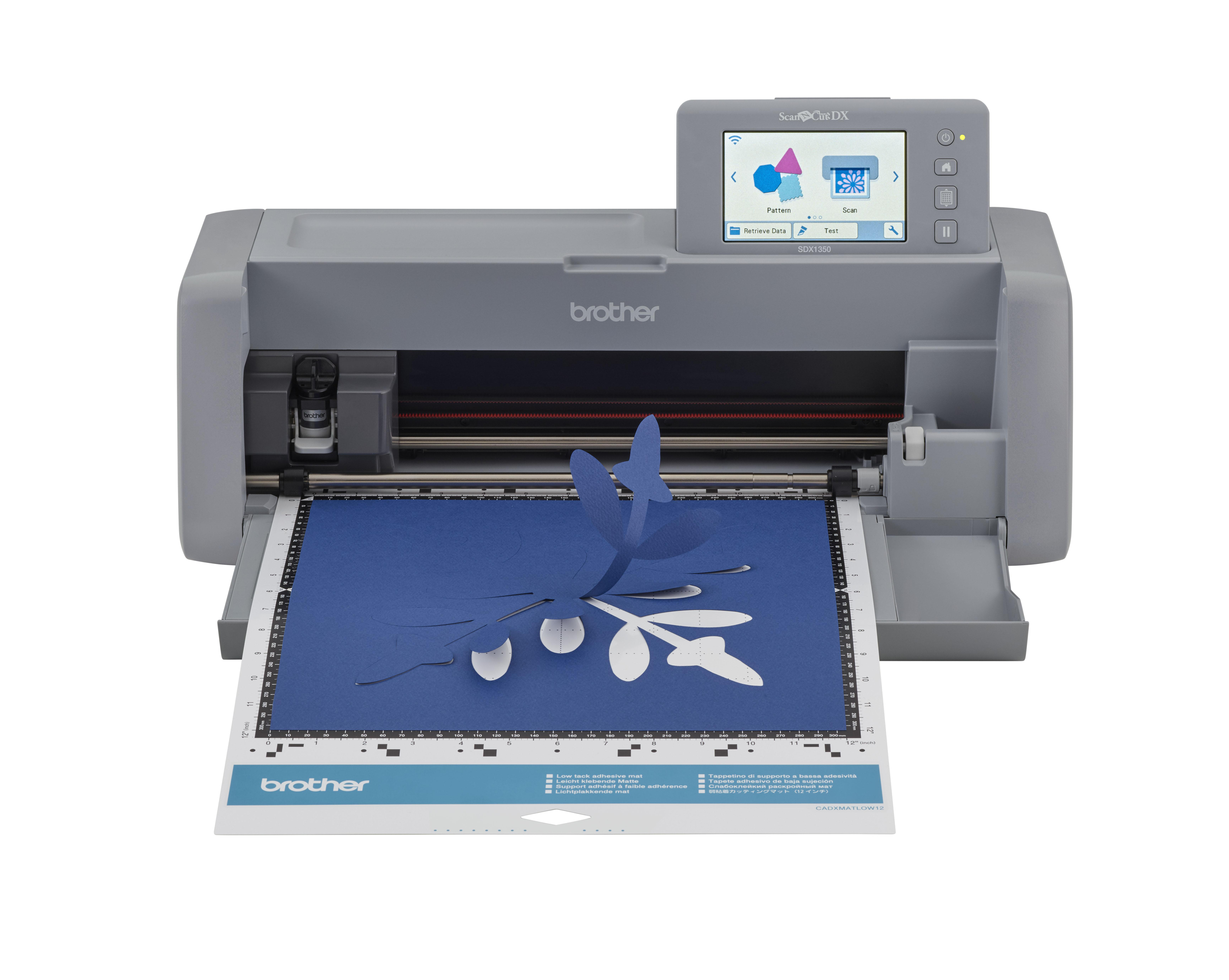 Eine Brother ScanNCut DX Maschine schneidet ein blaues Papier mit floralem Design. Weißer Hintergrund.