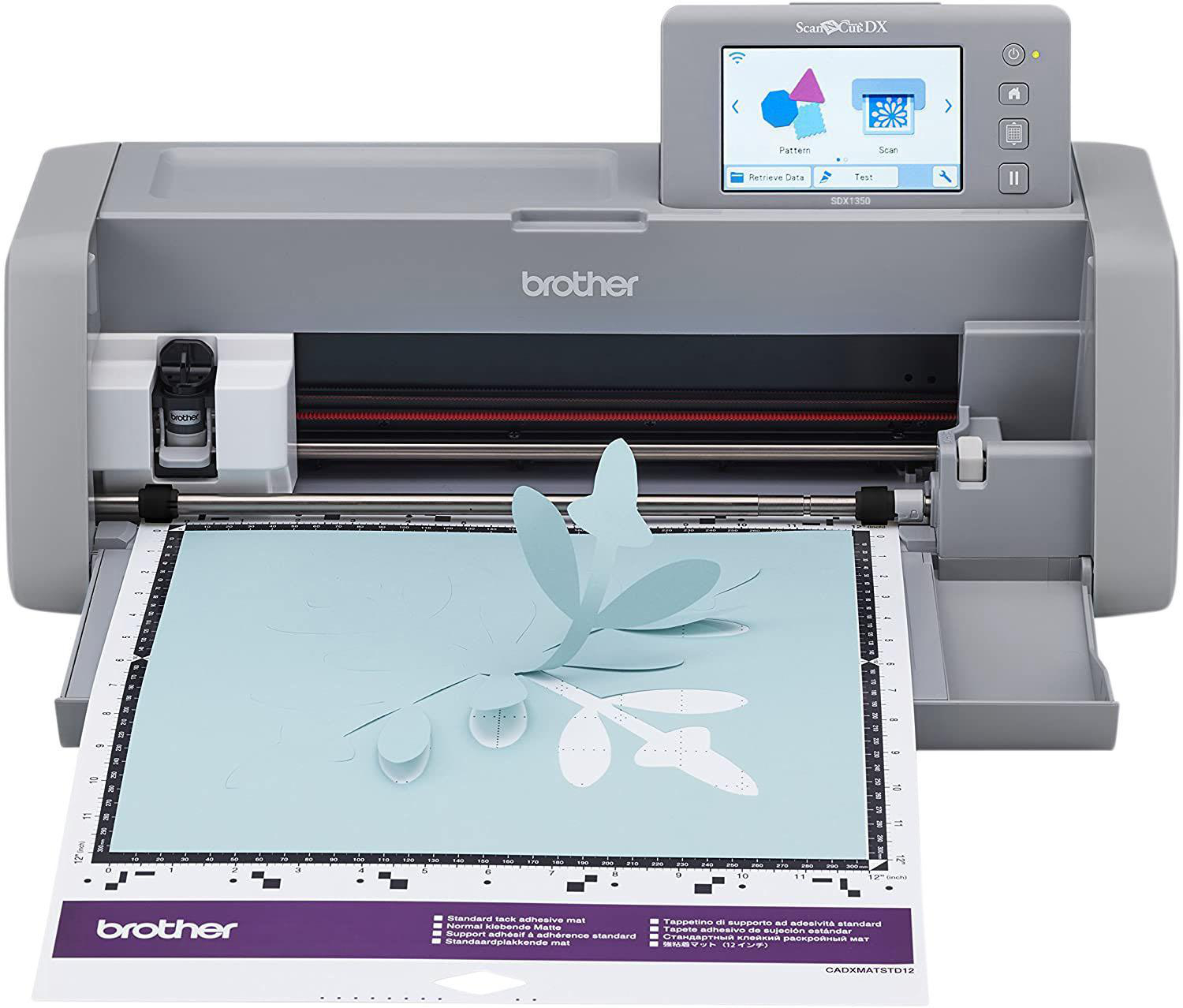 Brother ScanNCut DX Maschine. Ein blauer Papierauschnitt liegt auf der Matte. Graues Gehäuse mit Bildschirm.