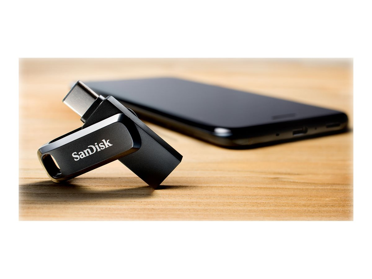 Ein schwarzer Sandisk USB-Stick neben einem schwarzen Smartphone auf einer Holzoberfläche. Der USB-Stick ist abgewinkelt.