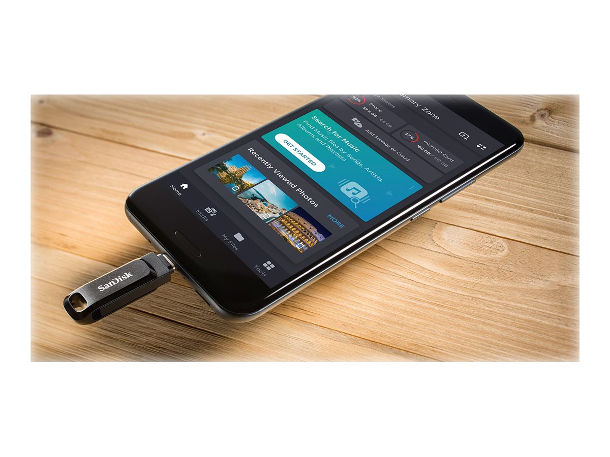Schwarzer SanDisk USB-Stick, der in ein schwarzes Smartphone auf einem Holztisch eingesteckt ist. Telefon zeigt eine App.