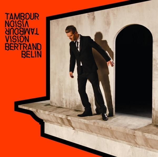 Pochette d'album avec un homme en costume debout sur un rebord. Fond et texte orange.