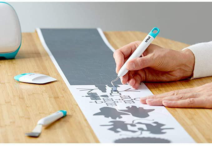 Person verwendet Cricut-Werkzeug, um ein Design auf einer grauen Oberfläche zu entgittern.