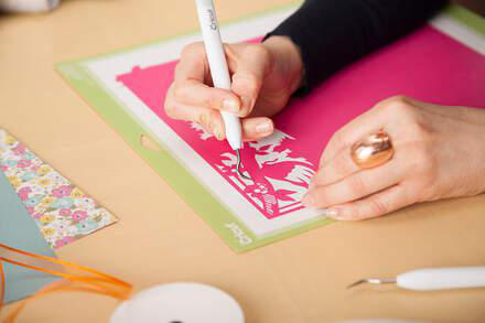 Hände schneiden rosa Papier auf grüner Matte mit Bastelmesser.