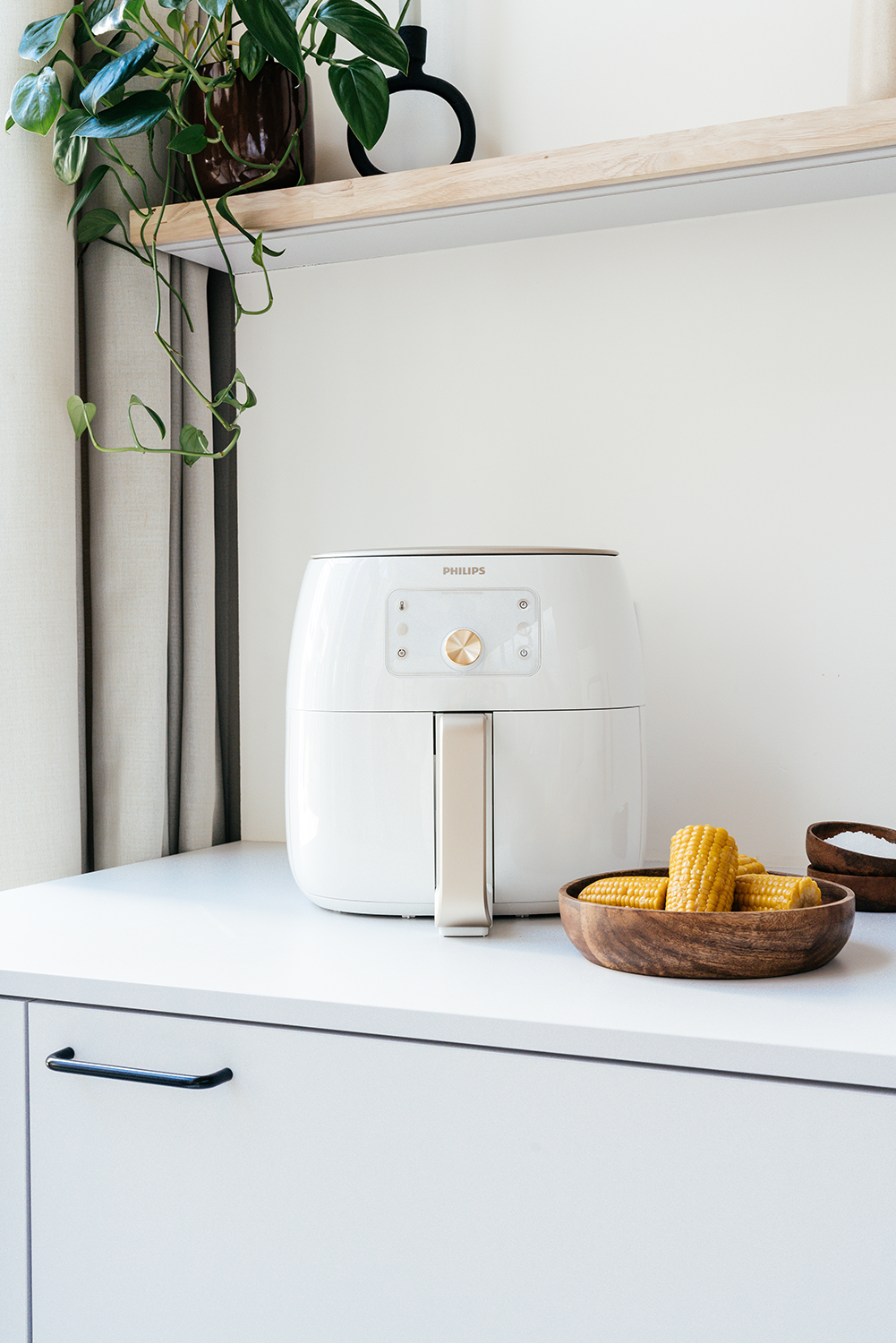 White air fryer on a white countertop, with corn on the cob in a wooden bowl.