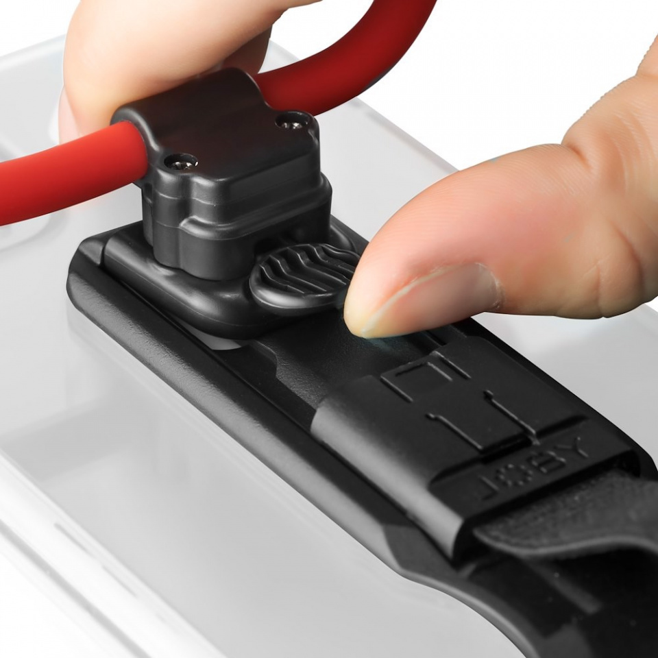 A hand pressing a clip into a black device with a red cable.