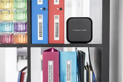 Een zwarte labelmaker op een plank met kleurrijke dozen en mappen met labels.