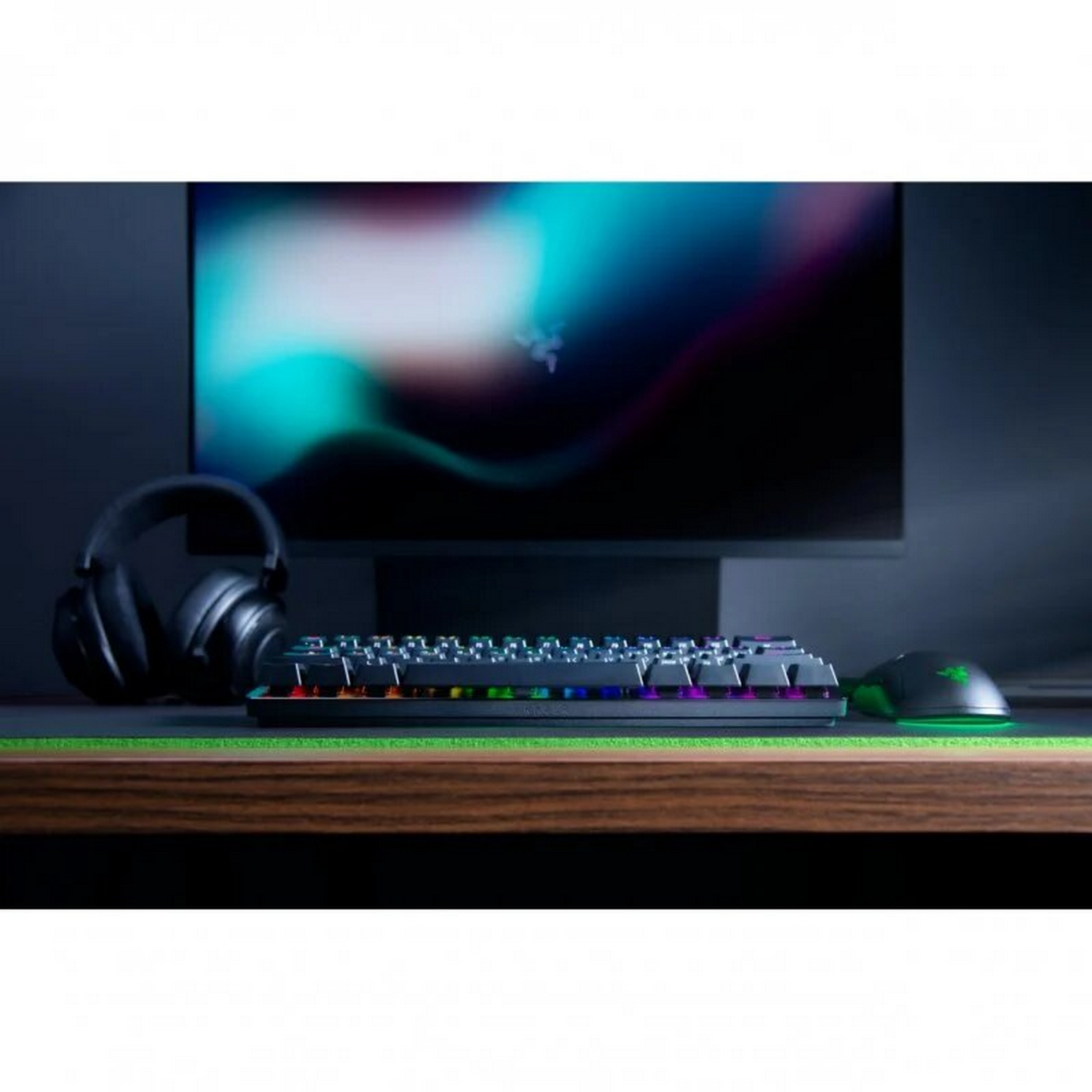 Una configuración de juego: teclado, ratón, auriculares y monitor, en un escritorio de madera con una alfombra verde.