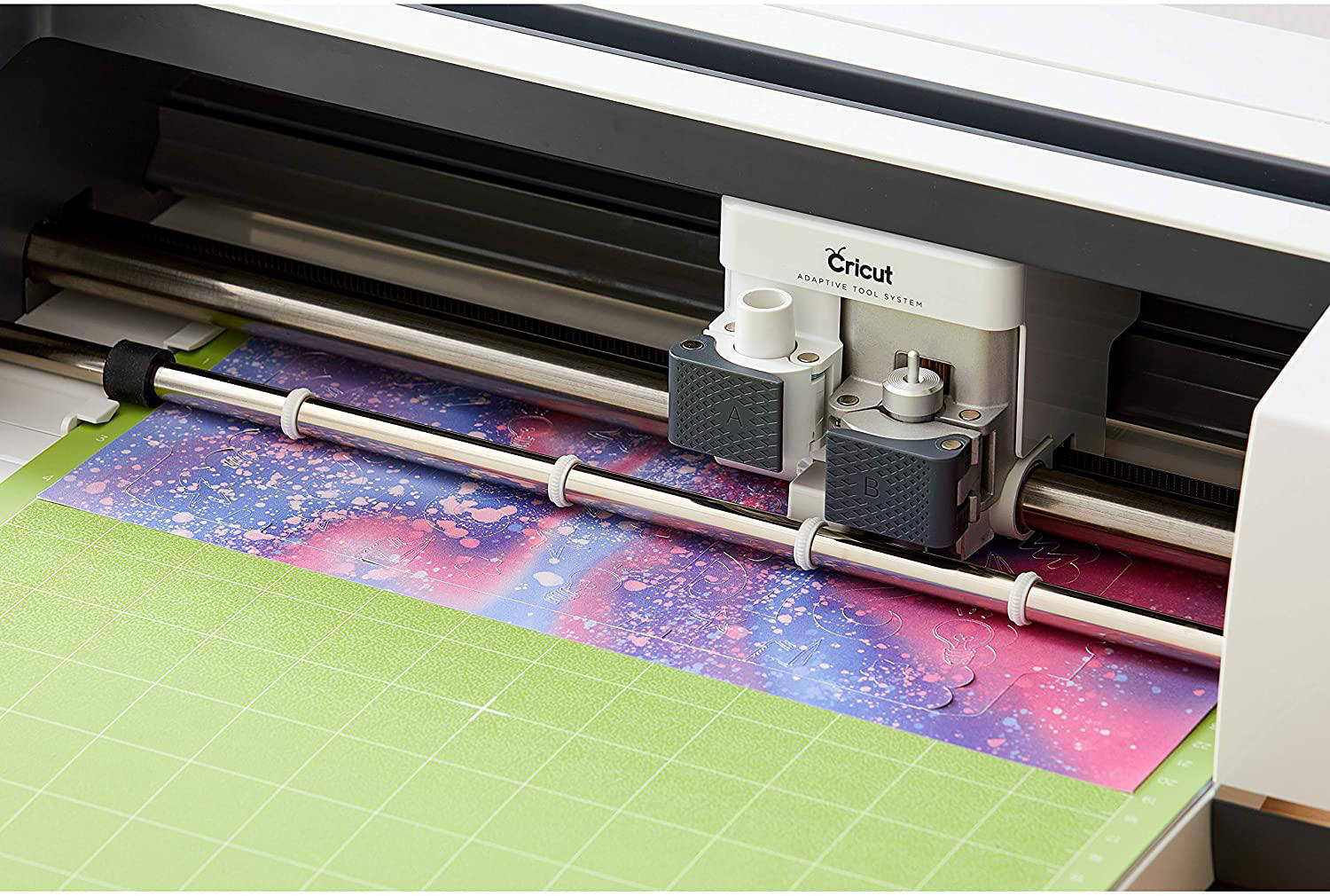 Cricut-Maschine schneidet buntes Papier auf einer grünen Matte. Maschine ist weiß. Nahaufnahme.