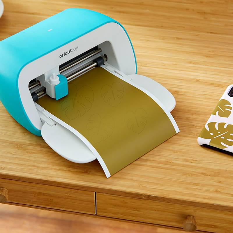 Eine blau-weiße Cricut Joy-Maschine, die Blattformen auf einem Holztisch schneidet.