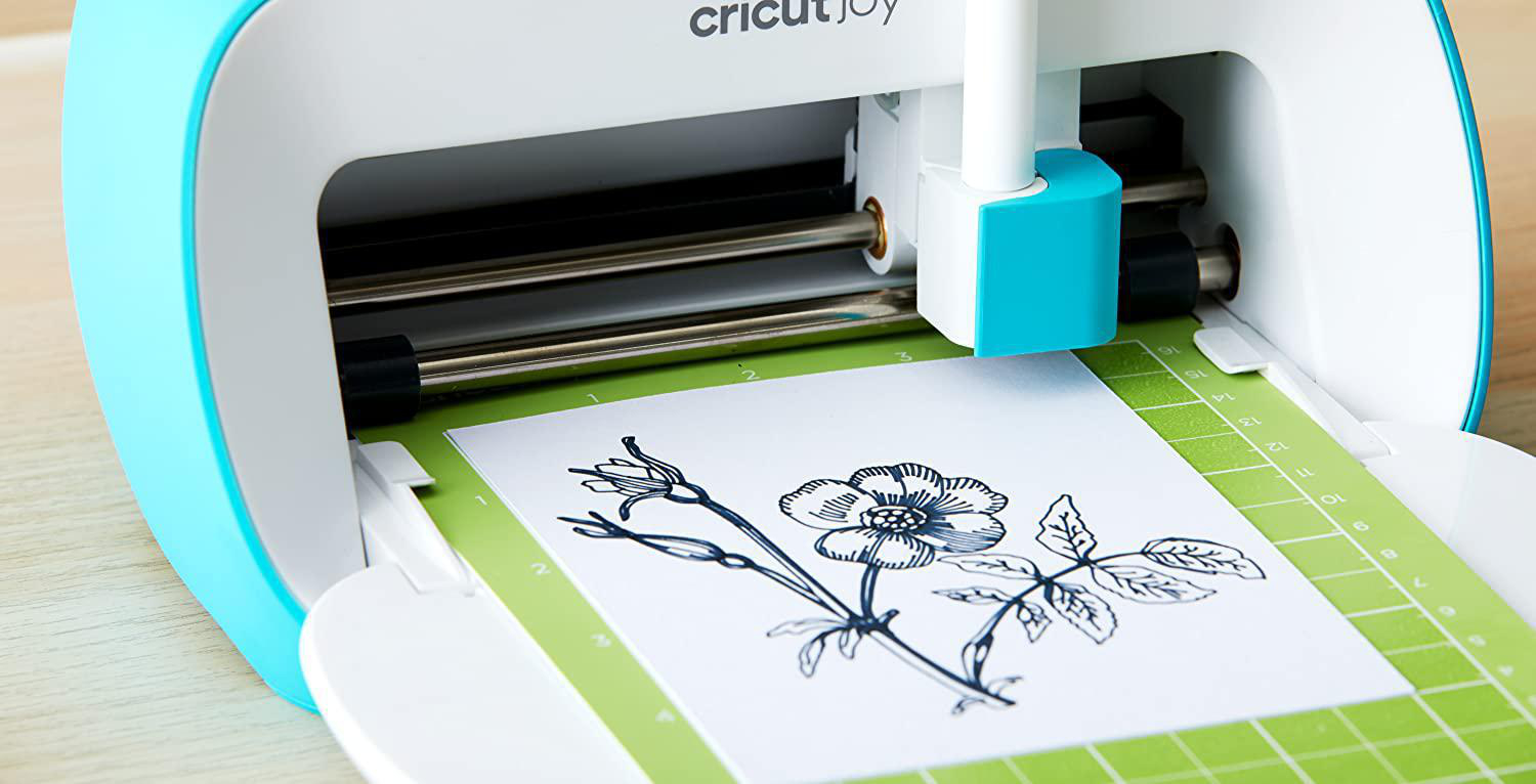 Eine Cricut Joy Maschine schneidet ein Blumendesign auf einer grünen Matte aus.