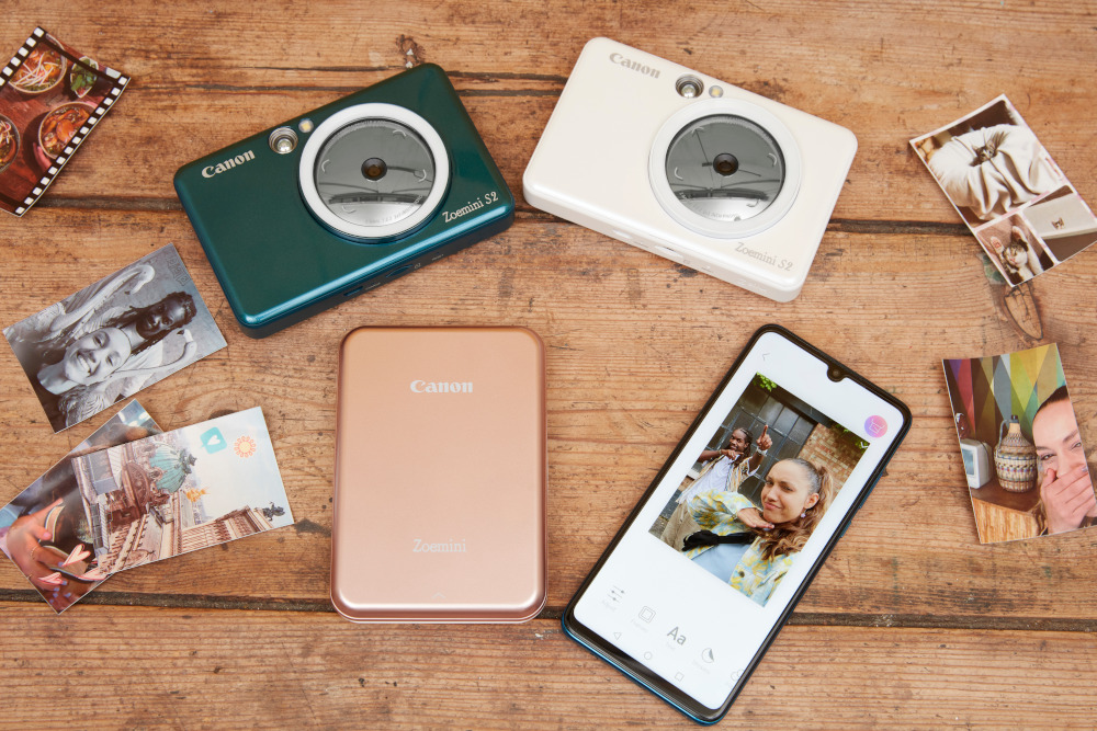 Four cameras and a smartphone on a wooden table, with photos scattered around the devices.