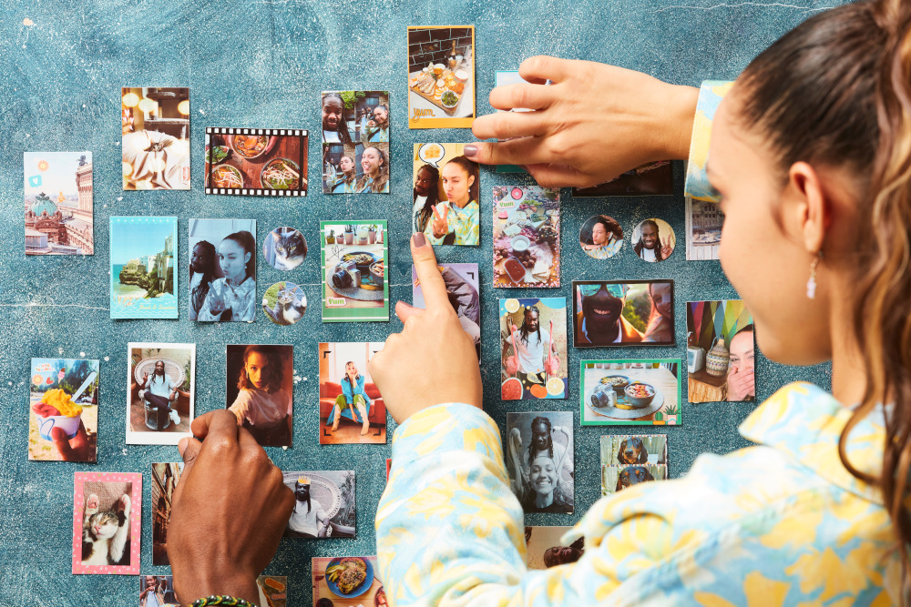 People arranging photos on a blue wall, with many pictures in frames of various sizes.
