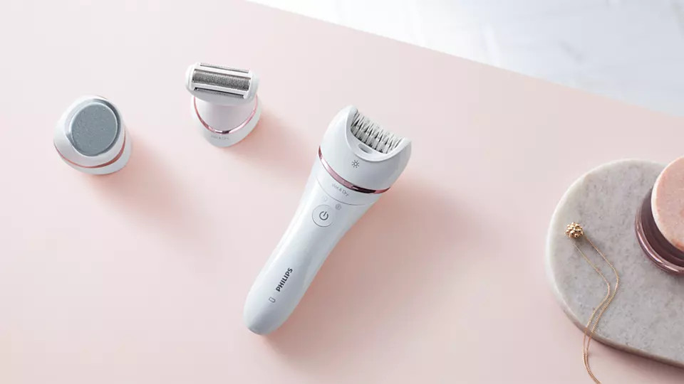White epilator and two other grooming tools on pink surface.