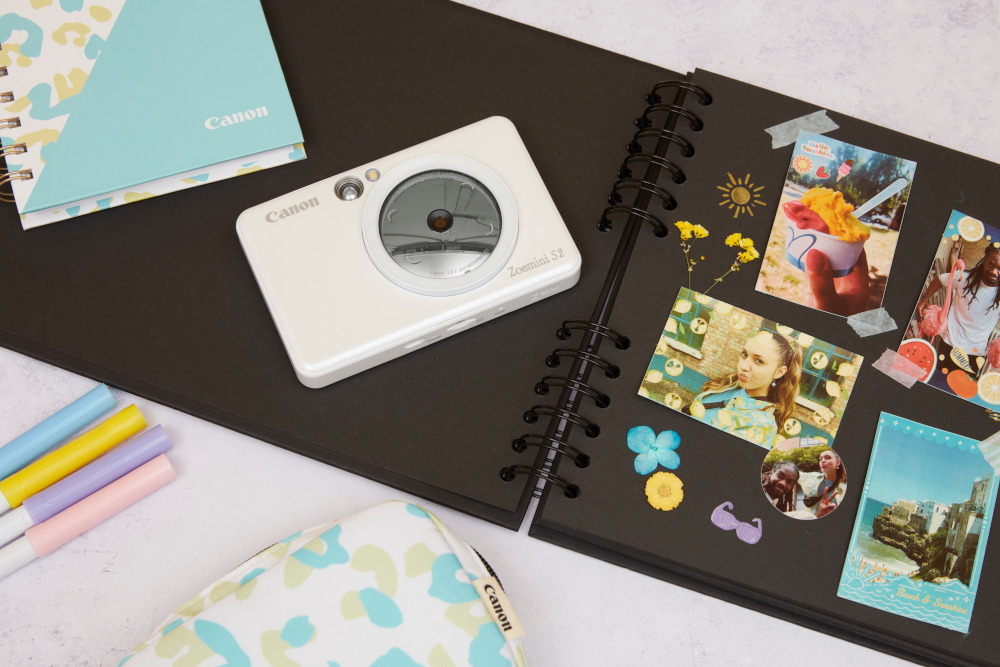 A Canon camera, photos, and pens on a black scrapbook.