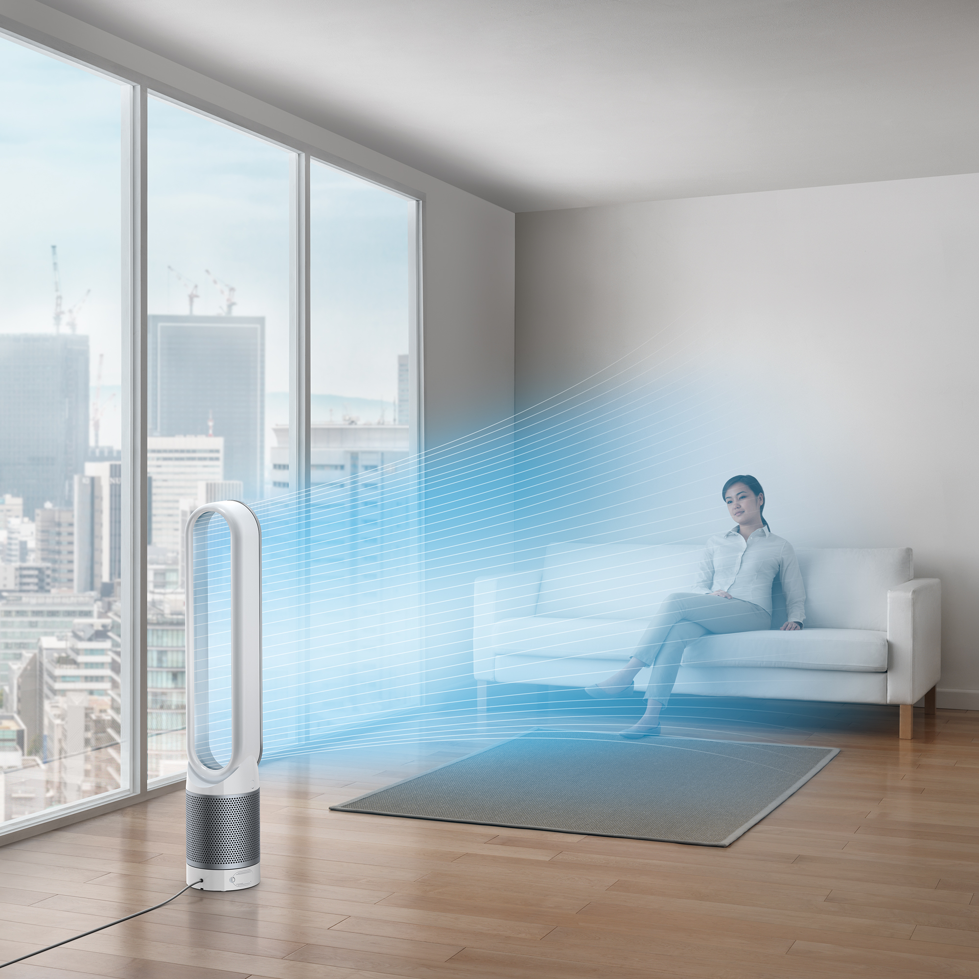 Een vrouw die bij een Dyson-ventilator zit met een stadsgezicht zichtbaar door een raam.