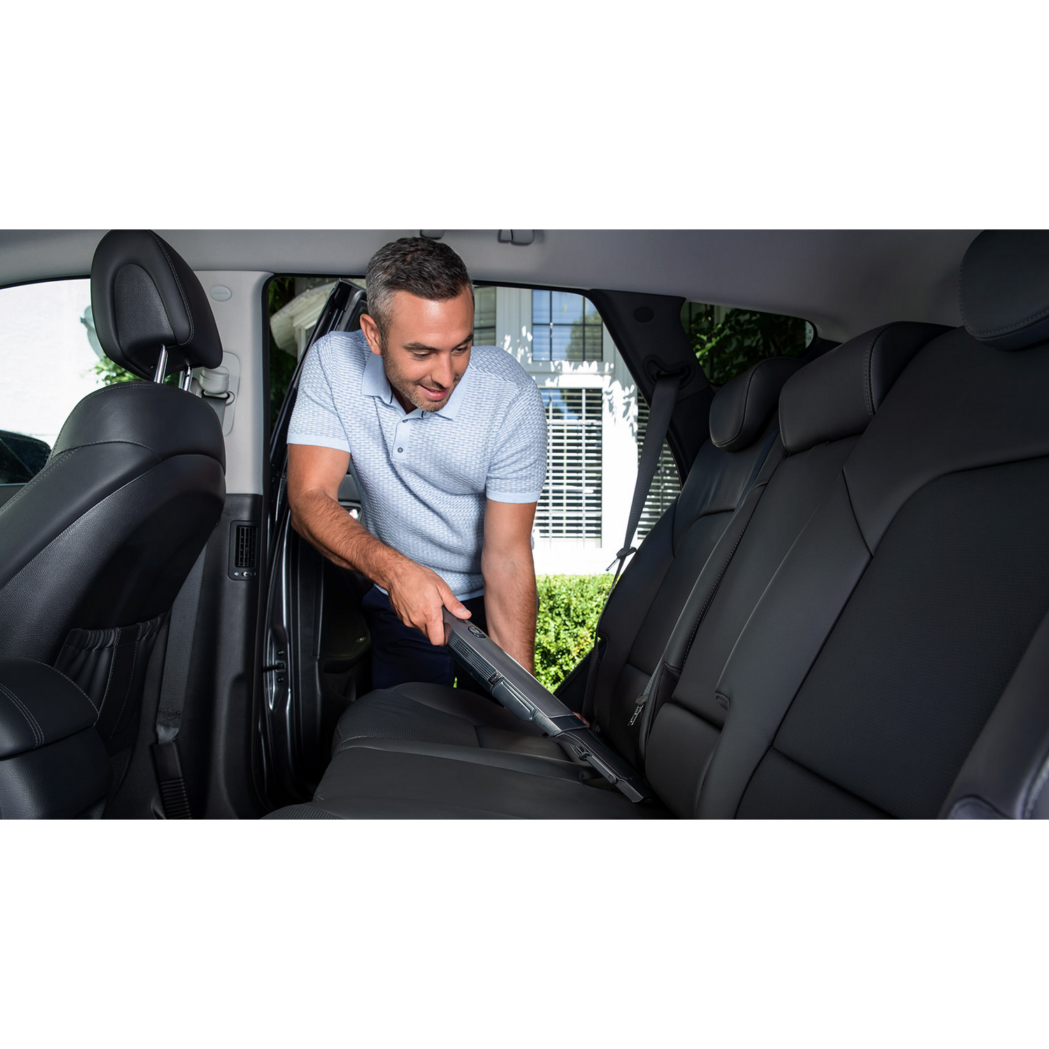 Un hombre aspira el asiento trasero de un coche, con una aspiradora de mano.