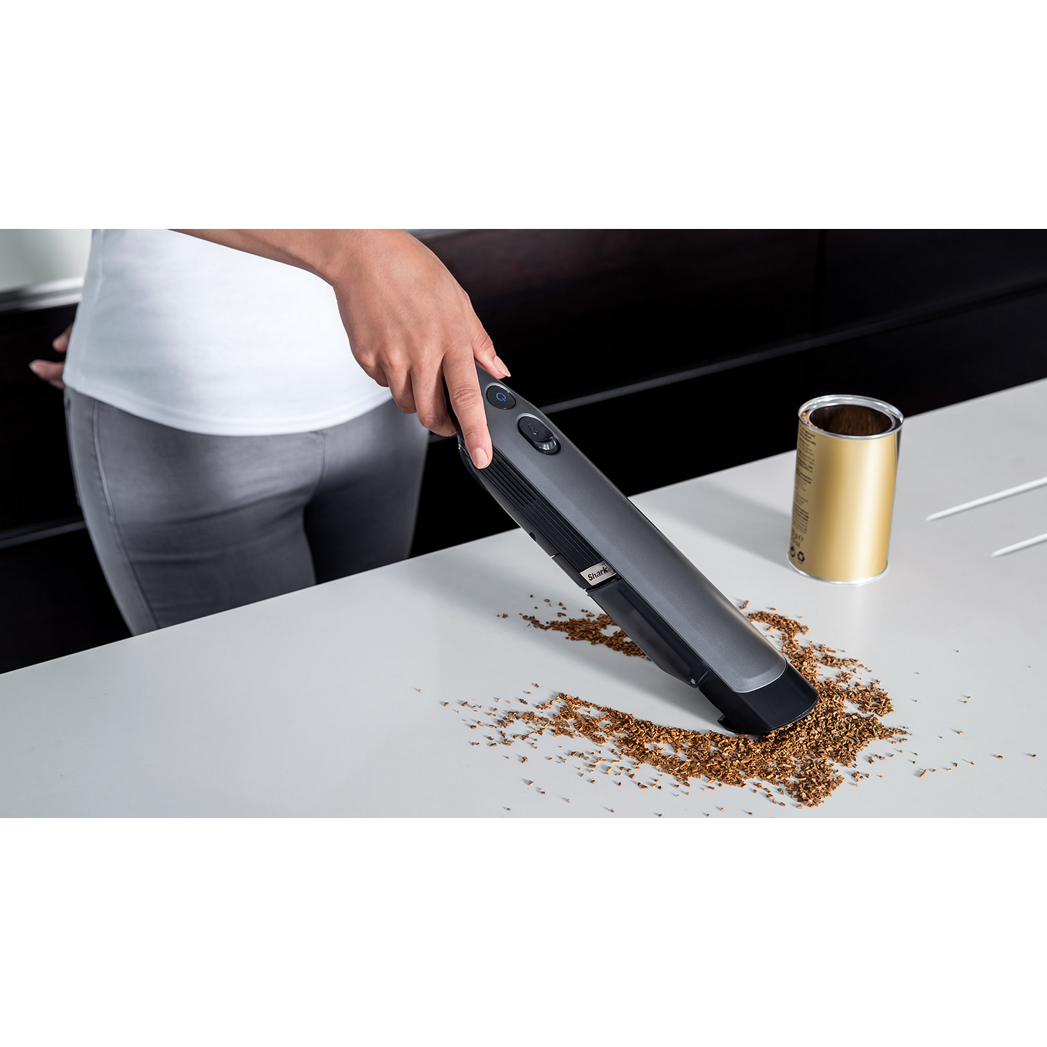 Una persona aspirando una mesa con una aspiradora de mano, con migas derramadas.