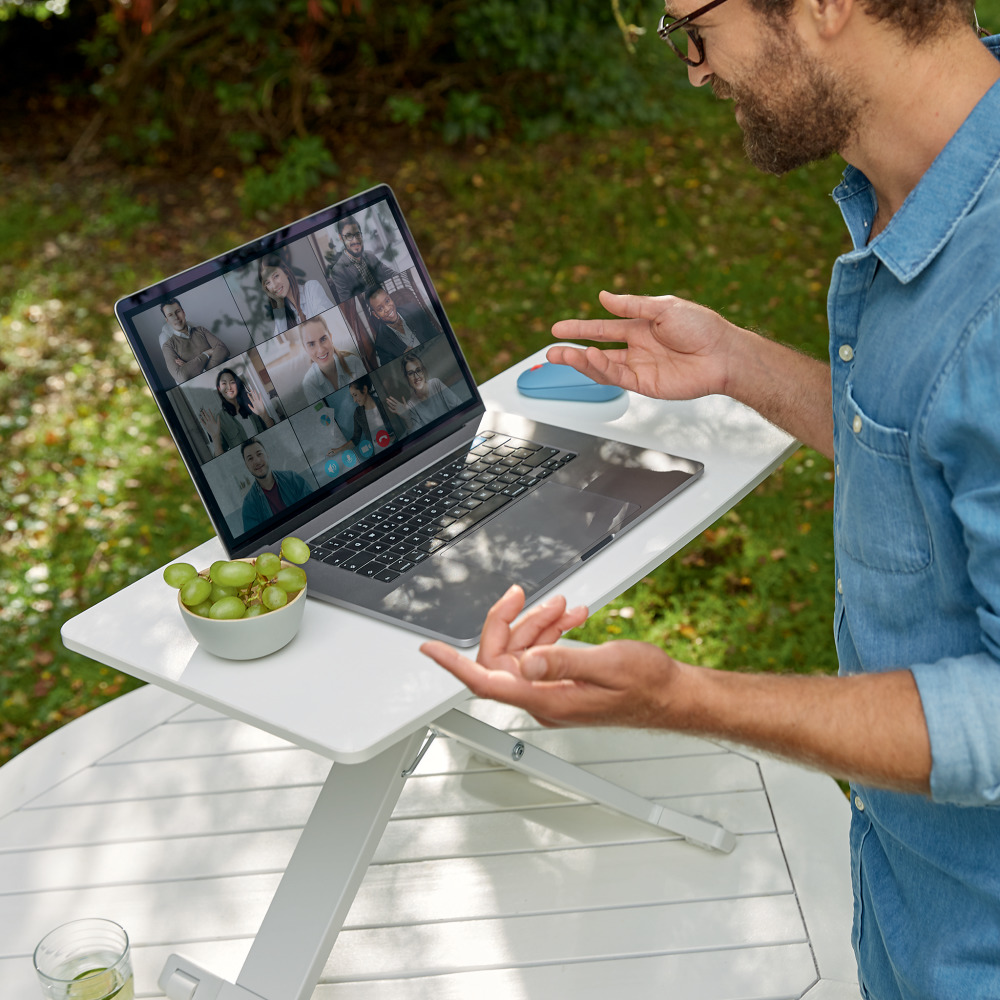 Egy kék inges férfi videokonferenciát tart a szabadban egy laptop segítségével.