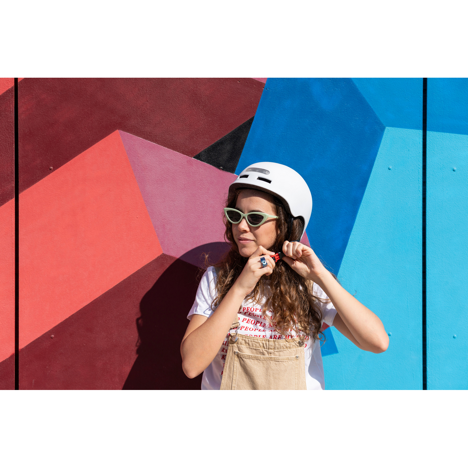 Mujer con casco blanco y gafas de sol ajustando la correa del casco.