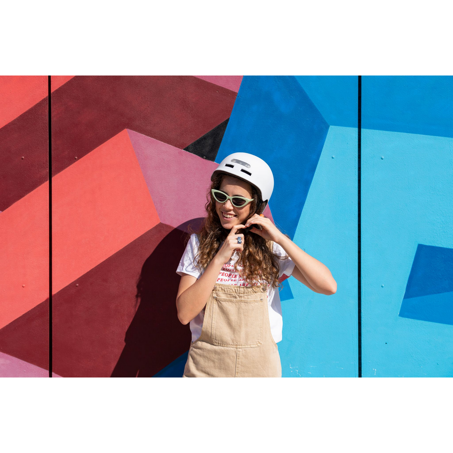Una mujer con casco blanco y mono sonríe frente a una pared colorida.
